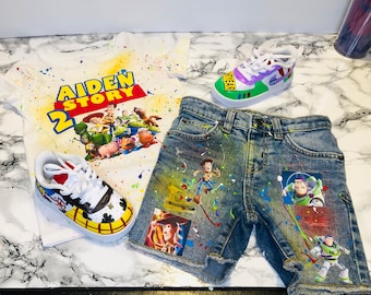 Puede incluir: Una camiseta blanca, unos pantalones cortos de mezclilla y dos pares de zapatillas con personajes de la película animada "Toy Story". La camiseta tiene el texto "AIDEN STORY 2" y salpicaduras de pintura coloridas. Los pantalones cortos y los zapatos también están decorados con imágenes de personajes.