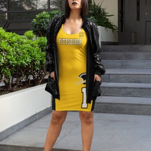 May include: A woman wearing a yellow and black jersey dress with the word "PITTSBURGH" on the front and a football helmet graphic on the side. She is wearing a black sequined jacket and nude heels.