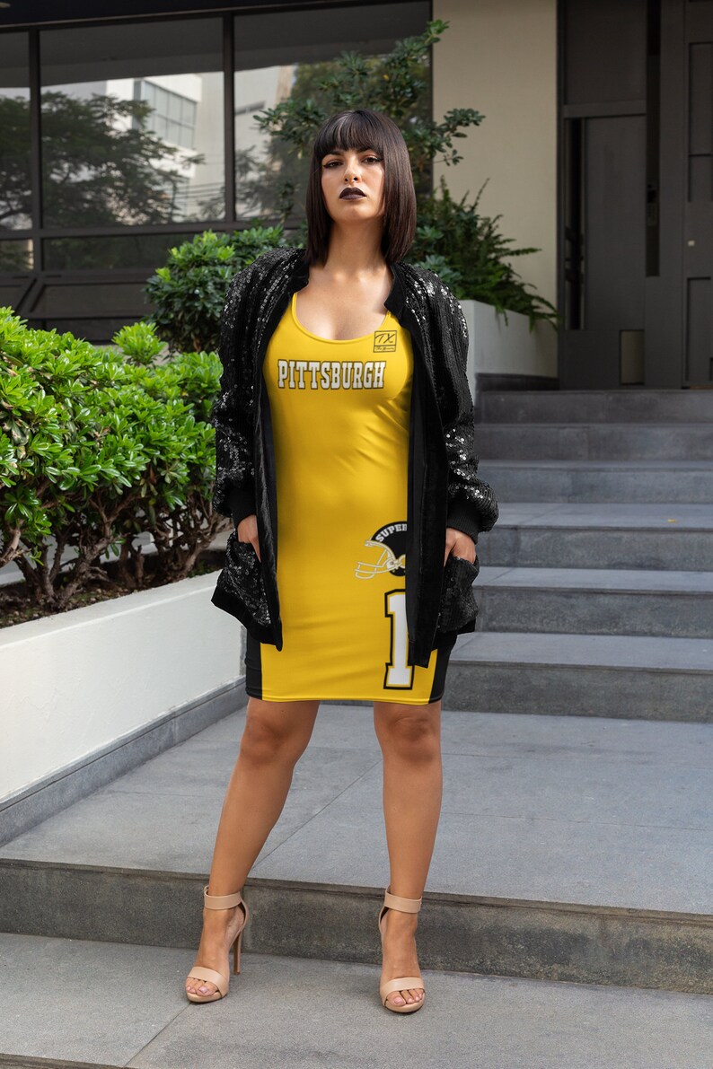 May include: A woman wearing a yellow and black jersey dress with the word "PITTSBURGH" on the front and a football helmet graphic on the side. She is wearing a black sequined jacket and nude heels.
