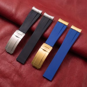以下が含まれることがあります： ゴム製の時計ストラップ2セット。1セットは黒で、シルバーカラーの金属製クラスプとエンドリンクが付いています。もう1セットは青で、ゴールドカラーの金属製クラスプとエンドリンクが付いています。各クラスプの表面には、小さな盾のロゴが刻印されています。