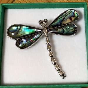 Könnte beinhalten: Eine silberne Libellenbrosche mit schillernden grünen und blauen Flügeln. Die Flügel sind aus Abalone-Schale.