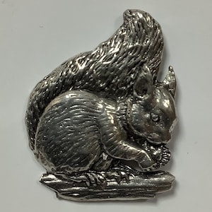 May include: A silver-colored squirrel figurine sitting on a log, holding a nut in its paws.