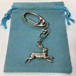 Puede incluir: Un llavero de plata con un dije de liebre y una bolsa de terciopelo azul. El dije está unido a un anillo partido de plata y un cierre de langosta de plata.