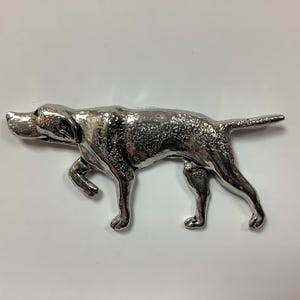 Könnte beinhalten: Eine silberfarbene Metallfigur eines Hundes in einer laufenden Pose. Der Hund ist mit einer strukturierten Oberfläche detailliert und hat einen langen Schwanz.