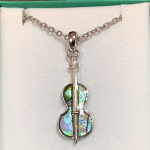 May include: A silver necklace with a cello pendant made of iridescent abalone shell. The cello is detailed with a silver string and a silver neck.
