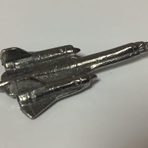 May include: A silver metal model of a SR-71 Blackbird aircraft. The model is detailed and shows the aircraft's distinctive shape.