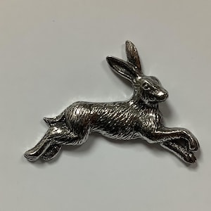 May include: A silver-coloured metal hare figurine in a running pose. The hare is detailed with fur texture and has long ears.
