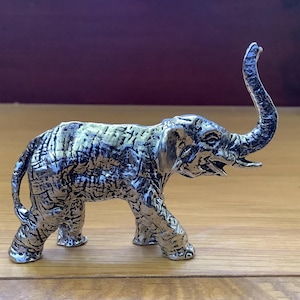 May include: A silver-colored elephant figurine with a textured surface. The elephant's trunk is raised in the air.