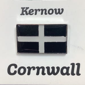 May include: A black and white enamel pin with the text "Kernow Cornwall" and a black and white flag design. The flag has a white cross on a black background.
