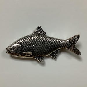 May include: A silver-colored fish figurine with detailed scales and a realistic design.