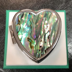 May include: A silver heart-shaped trinket box with a hinged lid. The box is decorated with an iridescent abalone shell inlay.