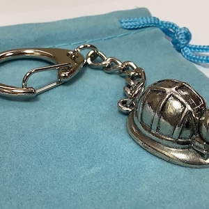 Könnte beinhalten: Ein silberner Schlüsselanhänger mit einem detaillierten Miniatur-Schutzhelm mit Licht. Der Schlüsselanhänger hat einen silbernen geteilten Ring und eine silberne Kette.