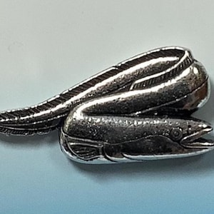 Pode incluir: Um alfinete de metal prateado que representa uma moreia enroscada em um círculo. A moreia é detalhada com escamas e uma superfície texturizada.