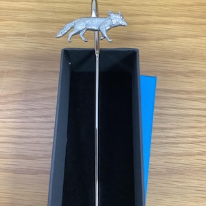 May include: Silver fox bookmark with a black velvet box. The bookmark is a thin metal rod with a fox figure at the top.