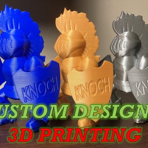 May include: Three 3D printed figurines of knights in blue, gold, and silver. Each knight is wearing armor and holding a shield with the word "KNOCH" embossed on it. The figurines are on a wooden surface with the text "CUSTOM DESIGN & 3D PRINTING" in front of them.