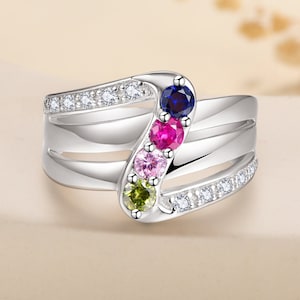 May include: A silver ring with a wave design, featuring a row of five colourful gemstones: blue, fuchsia, pink, light green, and yellow-green. The ring also has small white gemstones set along the band.