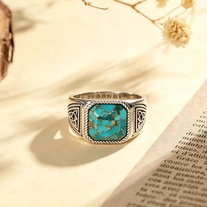 May include: A silver ring featuring a square-cut turquoise stone with brown matrix veining. The band is crafted with a rope-textured border around the stone and intricate triangular knotwork engravings on the sides of the metal shank.