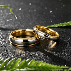 May include: Two rings featuring a two-tone design with a polished silver-colored center band and smooth gold-colored edges. The rings have a rounded profile and a reflective metallic finish, showcasing a clean and simple circular band construction.