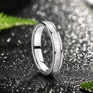 Peut inclure: Une bague en carbure de tungstène au ton argenté poli, dotée d'une incrustation blanche irisée et lisse centrée sur l'anneau. L'intérieur de la bague porte l'inscription gravée TUNGSTEN CARBIDE, présentant une finition métallique réfléchissante.