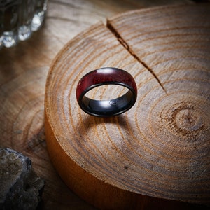 May include: A black and red ring with a wood inlay. The ring is sitting on a wooden surface.