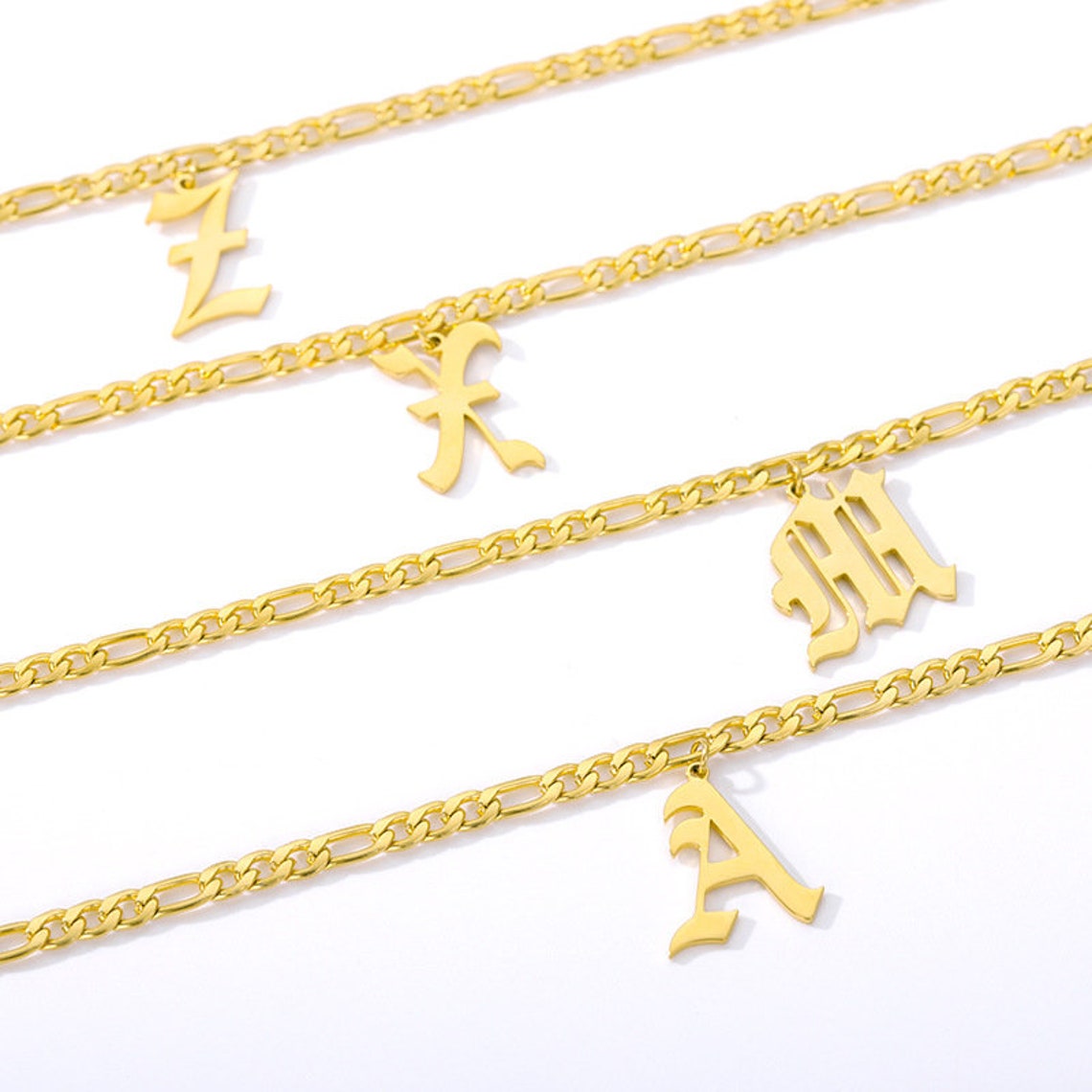 May include: Three gold chains with different letter charms. The charms are in an old English font. The letters are "L", "F", "M", and "A".