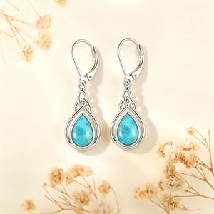 May include: A pair of silver leverback earrings featuring a teardrop-shaped turquoise stone set within a polished metal frame. The design includes an intricate knotwork detail above the stone, creating a balanced and symmetrical appearance.