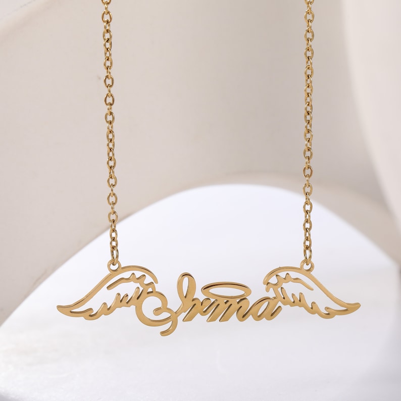 Puede incluir: Collar de oro con una placa de nombre que dice "Shana" con alas de &aacute;ngel y un halo.