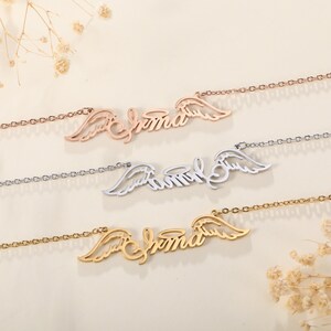 Puede incluir: Tres collares en oro, plata y oro rosa, cada uno con el nombre "Emma" escrito en cursiva con alas de &aacute;ngel a cada lado.