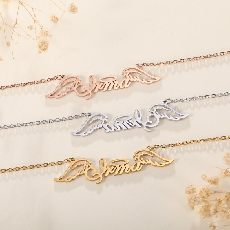 Puede incluir: Tres collares en oro, plata y oro rosa, cada uno con el nombre "Emma" escrito en cursiva con alas de &aacute;ngel a cada lado.