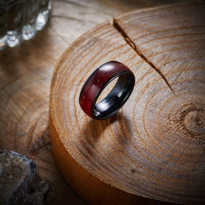 May include: A black and red ring with a wooden inlay. The ring is sitting on a wooden surface.