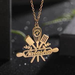 May include: Gold necklace with a pendant featuring a rolling pin, spatula, whisk, and a heart with the name "Natasha" on it.