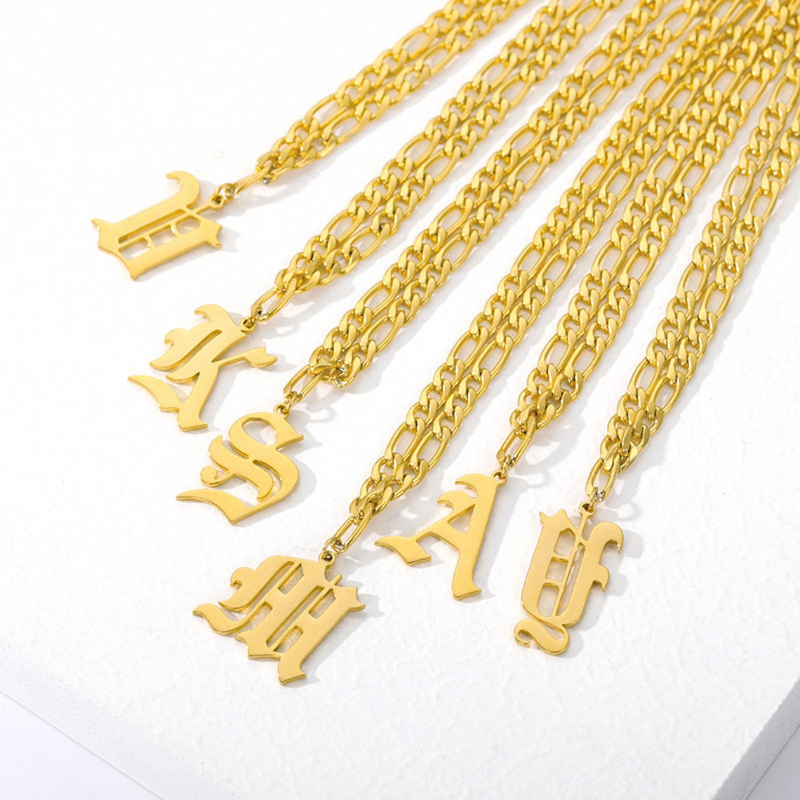 May include: Gold chain necklaces with letter charms. The charms are in an old English font. The chains are of different widths and styles.