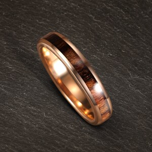 May include: A rose gold wedding band with a dark brown wood inlay.