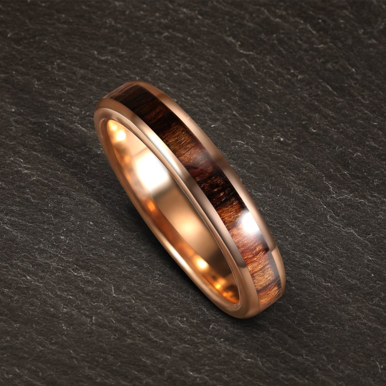 May include: A rose gold wedding band with a dark brown wood inlay.