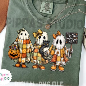 Könnte beinhalten: Salbeigrünes Comfort Colors T-Shirt mit Halloween-Design. Drei Geisterfiguren in Patchwork-Outfits halten einen Kürbis-Korb, eine schwarze Katze und ein "Trick or Treat"-Schild. Das Shirt hat den Text "Pippas Studio" und "Digital PNG File".