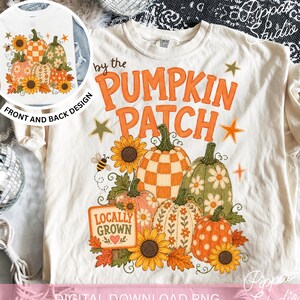 May include: An off-white t-shirt featuring a graphic of pumpkins, sunflowers, and a bee. The text reads by the PUMPKIN PATCH and LOCALLY GROWN. The design includes a checkered pumpkin, a floral green pumpkin, and orange pumpkins with stars.