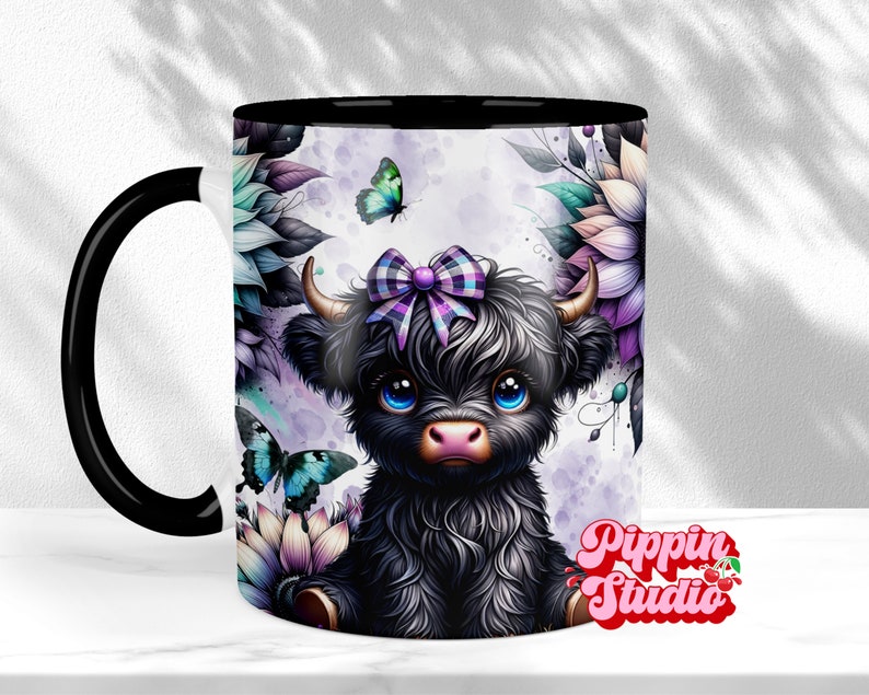 K&ouml;nnte beinhalten: Keramikbecher mit schwarzem Innenraum und Henkel, mit einer Illustration einer schwarzen Highland-Kuh mit lila Schleife, umgeben von Blumen und Schmetterlingen. Der Becher hat den Text "Pippin Studio" in rosa Schrift.