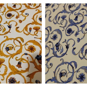 May include: Two fabric swatches with a white background and a repeating pattern of gold and blue floral designs. The designs are intricate and feature swirling vines and flowers.