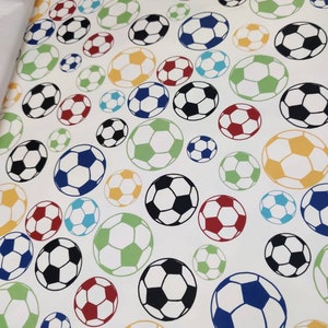 May include: White fabric with a repeating pattern of colourful footballs. The footballs are in various colours, including red, blue, green, yellow, and black.