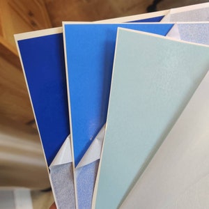 May include: Four sheets of adhesive paper in various shades of blue. The sheets are stacked on top of each other, with the top sheet being a light blue, the second sheet being a darker blue, and the bottom two sheets being a deep blue.
