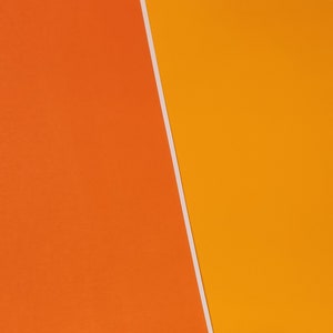 May include: A close-up of two pieces of paper, one orange and one yellow, meeting at a diagonal line.