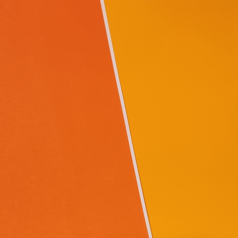 May include: A close-up of two pieces of paper, one orange and one yellow, meeting at a diagonal line.