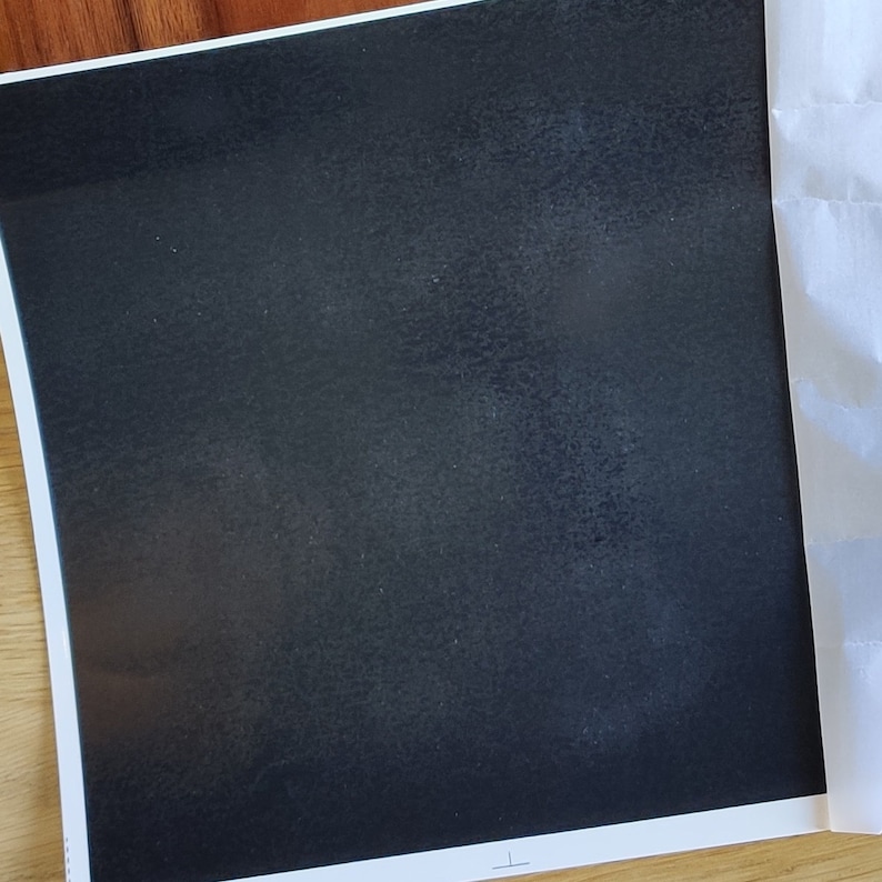 May include: A black square piece of paper with a slightly textured surface.