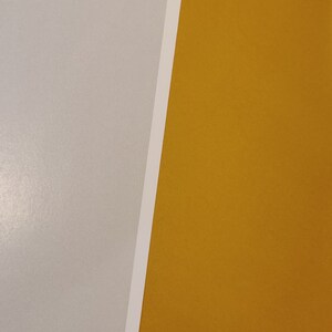 May include: A close-up of two pieces of paper, one is a light gray and the other is a bright yellow.