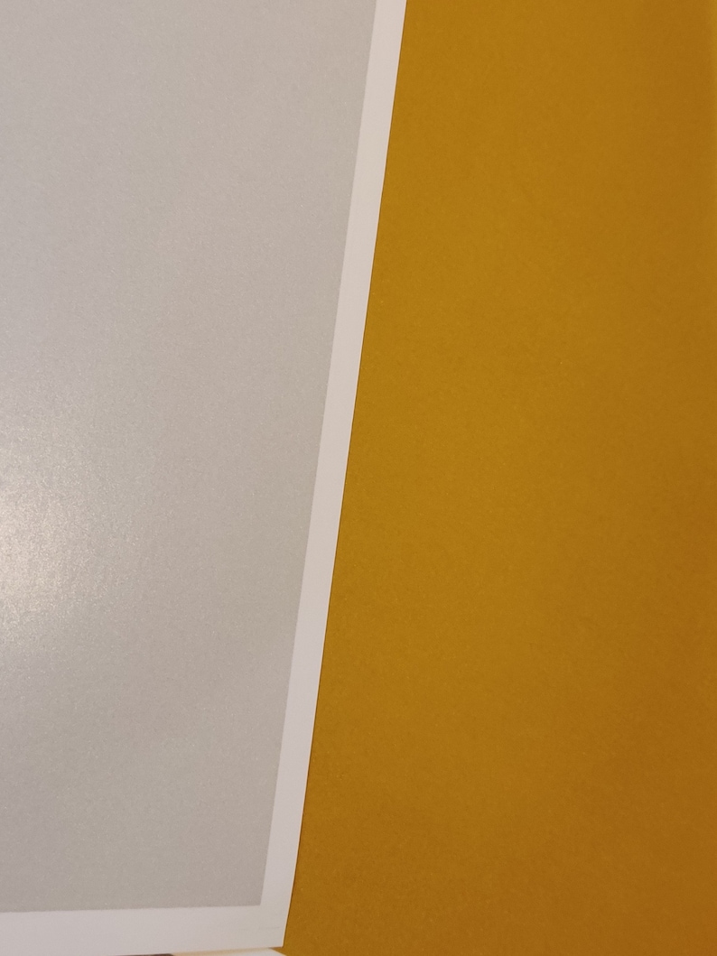 May include: A close-up of two pieces of paper, one is a light gray and the other is a bright yellow.