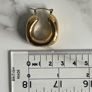 Op de afbeelding: Gouden creolen met een diameter van ongeveer 2 cm. De oorbellen zijn dik en hebben een afgeronde, licht ovale vorm.