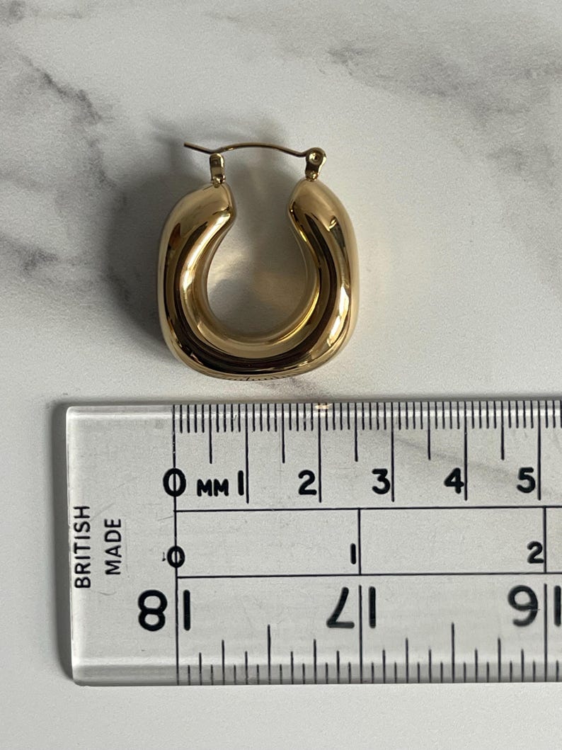Op de afbeelding: Gouden creolen met een diameter van ongeveer 2 cm. De oorbellen zijn dik en hebben een afgeronde, licht ovale vorm.