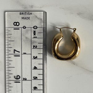 Op de afbeelding: Gouden creolen met een dik, afgerond ontwerp. De oorbellen zijn ongeveer 2,5 cm in diameter.