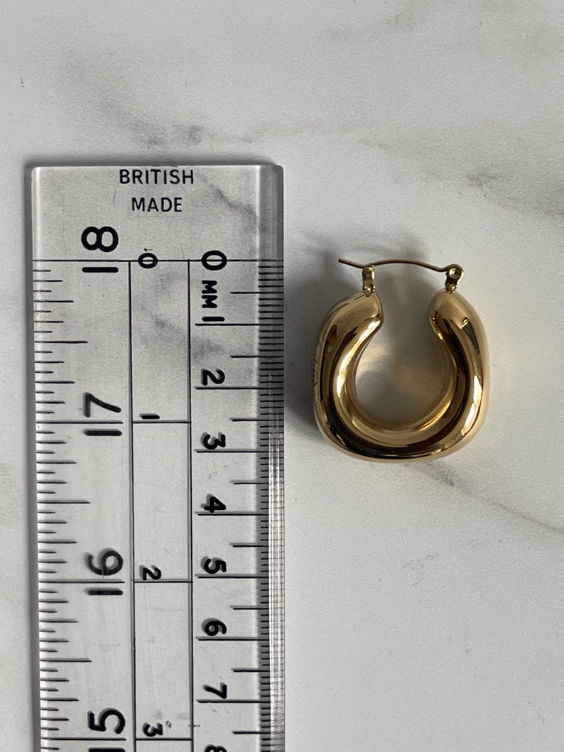 Op de afbeelding: Gouden creolen met een dik, afgerond ontwerp. De oorbellen zijn ongeveer 2,5 cm in diameter.