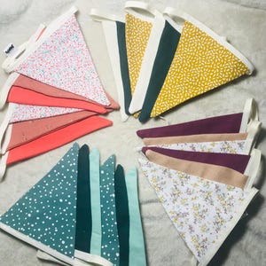 May include: A set of colourful fabric triangle flags with various patterns, including floral, polka dot and geometric designs. The flags are strung together with white ribbon and have a white border.
